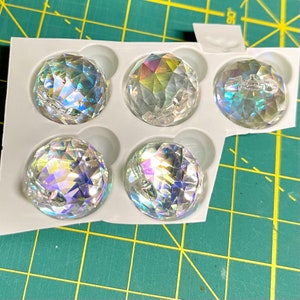 K&ouml;nnte beinhalten: F&uuml;nf schimmernde, klare Glassph&auml;ren in einer wei&szlig;en Kunststoffschale. Die Sph&auml;ren sind in einem Raster angeordnet.