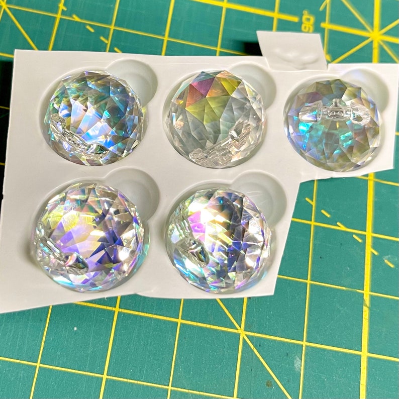 K&ouml;nnte beinhalten: F&uuml;nf schimmernde, klare Glassph&auml;ren in einer wei&szlig;en Kunststoffschale. Die Sph&auml;ren sind in einem Raster angeordnet.