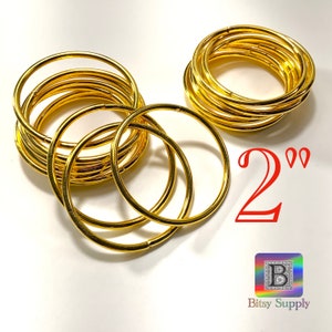 May include: Two sets of 10 gold-coloured metal hoops, each measuring 2 inches in diameter. The hoops are stacked on top of each other. The text "2"" is written in red below the hoops. The text "Bitsy Supply" is written in black below the red text.