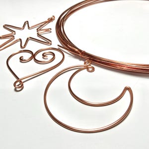May include: Copper wire shapes including a star, heart, and crescent moon. A bundle of copper wire is also present. The shapes are made from copper wire and are arranged on a white surface. The star has multiple points.