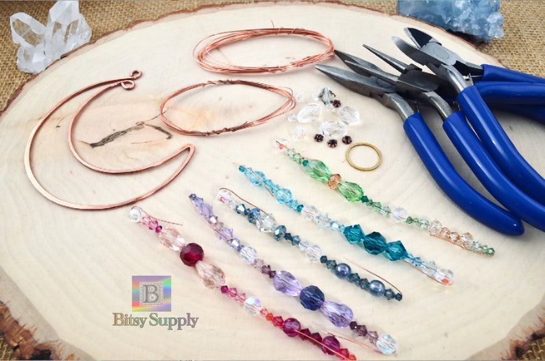 May include: A set of jewelry making supplies including copper wire, crystal beads, and pliers. The beads are arranged in rainbow colors on a wooden surface. The text "Bitsy Supply" is visible in the bottom left corner of the image.