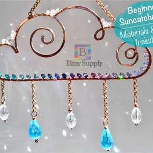 Op de afbeelding: Een beginnersset voor het maken van een zonenvanger met een wolk van koperdraad versierd met iriserende kralen en hangende traanvormige kristallen. De set bevat alle materialen en gereedschappen die nodig zijn om de zonenvanger te maken.  "Beginner Suncatcher Kit Materials & Tools Included!" staat in witte tekst op een turquoise cirkel.