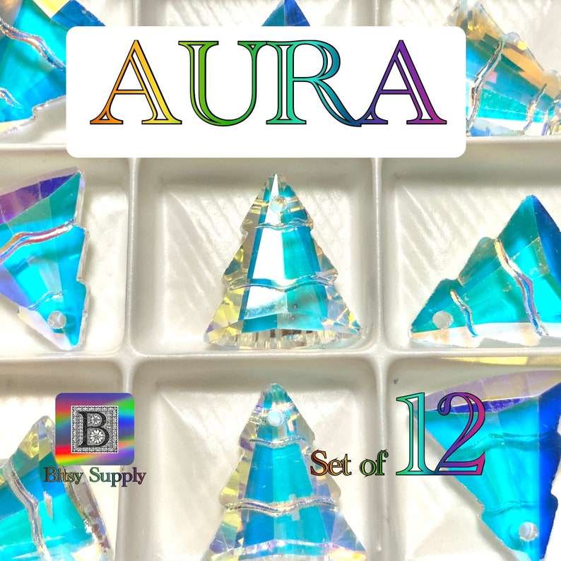 May include: Set of 12 iridescent blue crystal Christmas tree charms. The charms are in a clear plastic container with the word "AURA" in rainbow letters at the top. The charms are labeled "Set of 12" and "Bitsy Supply" in the bottom left corner.