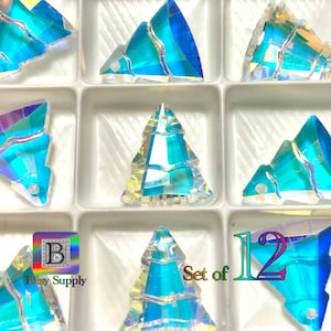 May include: Set of 12 iridescent blue and clear glass Christmas tree shaped embellishments. The embellishments are in a clear plastic container with a white background. The text "Set of 12" is visible in the image.