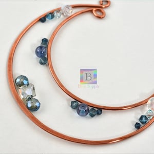 May include: Copper wire crescent moon with blue and clear glass beads. The crescent moon is made of two pieces of wire, one inside the other. The beads are scattered around the moon.