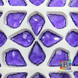 Peut inclure: Gros plan d'un plateau rempli de plusieurs pendentifs en cristal violets en forme de goutte d'eau. Chaque pendentif a un bord festonn&eacute; et est plac&eacute; dans un compartiment blanc. Les cristaux sont d'une teinte violette vibrante.