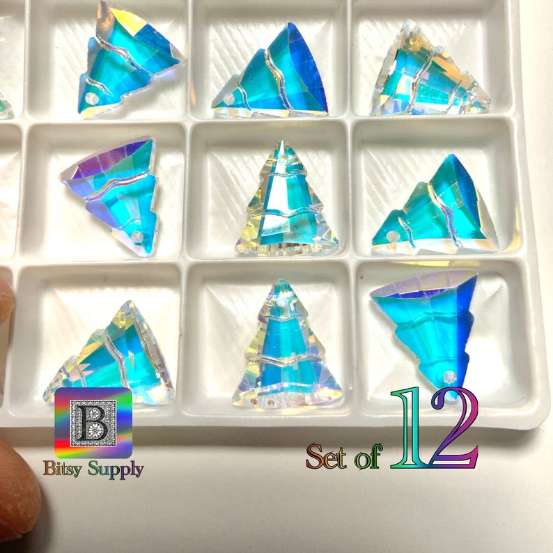 May include: A set of 12 iridescent blue crystal Christmas tree charms. The charms are arranged in a clear plastic storage box. The box has a white background and the text "Set of 12" is printed on the bottom right corner.