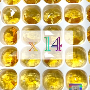Puede incluir: Primer plano de una bandeja blanca llena de 14 cuentas de vidrio transparentes, facetadas y de color &aacute;mbar. Las cuentas est&aacute;n dispuestas en forma de cuadr&iacute;cula y tienen un agujero en el centro. El texto "X 14" est&aacute; impreso en letras moradas y azules en el centro de la bandeja.