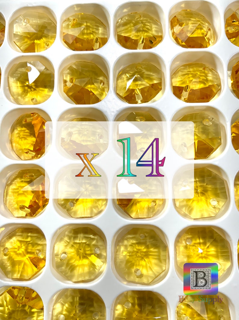 Puede incluir: Primer plano de una bandeja blanca llena de 14 cuentas de vidrio transparentes, facetadas y de color &aacute;mbar. Las cuentas est&aacute;n dispuestas en forma de cuadr&iacute;cula y tienen un agujero en el centro. El texto "X 14" est&aacute; impreso en letras moradas y azules en el centro de la bandeja.