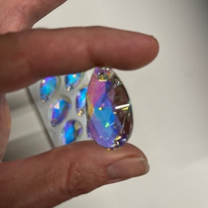 May include: A teardrop-shaped crystal prism with iridescent rainbow colors. The prism is clear and has a faceted design.