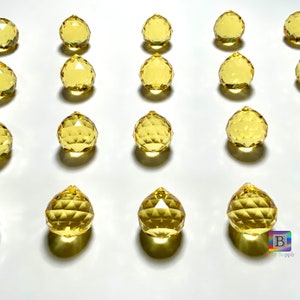May include: A collection of 15 yellow crystal ball prisms, each with a faceted design, arranged in rows on a white surface.
