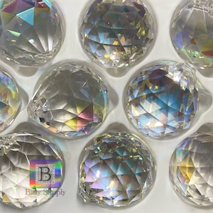 May include: A close-up of a package of 10 clear crystal faceted balls. The balls are iridescent and have a rainbow effect. The balls are in a white foam packaging.
