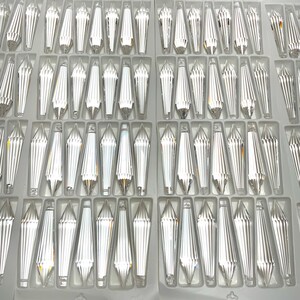 May include: A close-up view of a clear crystal prism, with a faceted design, arranged in rows on a white background. The prisms are all the same size and shape, and they are arranged in a grid pattern.