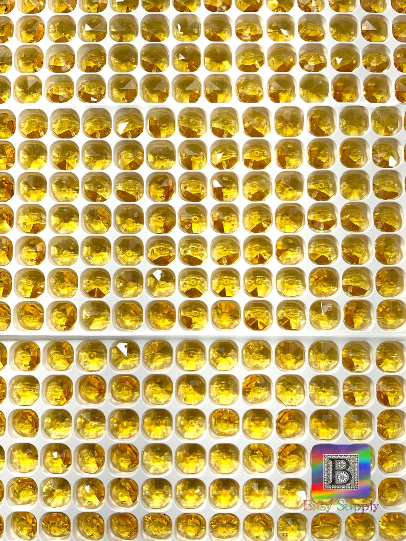 Puede incluir: Una vista cercana de una l&aacute;mina de pl&aacute;stico transparente con muchos compartimentos cuadrados peque&ntilde;os. Cada compartimento contiene un solo cristal de imitaci&oacute;n de vidrio facetado de color &aacute;mbar. Los cristales de imitaci&oacute;n est&aacute;n dispuestos en filas y columnas.