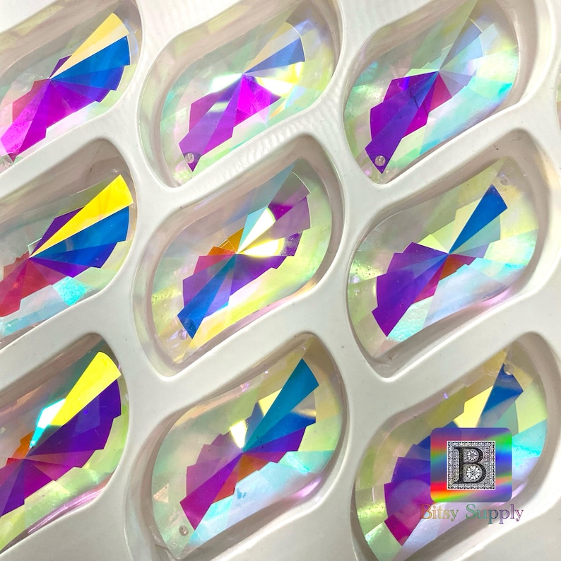 Puede incluir: Primer plano de una l&aacute;mina de piedras de cristal ovaladas iridiscentes, de colores arco&iacute;ris. Las piedras de cristal est&aacute;n dispuestas en filas en una bandeja de pl&aacute;stico transparente. Todas las piedras de cristal son del mismo tama&ntilde;o y forma. La bandeja est&aacute; etiquetada con "Bitsy Supply".