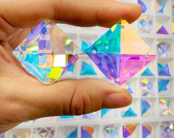 Peut inclure: Deux cristaux de verre carrés irisés avec un effet arc-en-ciel. Les cristaux sont tenus dans une main sur un fond de nombreux cristaux similaires.
