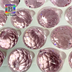 Può includere: Primo piano di un pacchetto di ornamenti a forma di sfera di cristallo rosa. Le sfere sono disposte in un vassoio di schiuma bianca. Le sfere sono sfaccettate e hanno una finitura lucida.