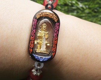 May include: A red beaded bracelet with a silver charm and a black and gold amulet featuring a small golden figure inside a clear glass case.