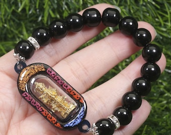 May include: Black beaded bracelet with a silver charm featuring a gold-colored figure in a colorful frame.