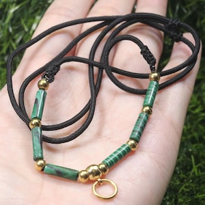 Puede incluir: Un collar de cordón negro con un cierre dorado y cuentas rayadas verdes y negras.