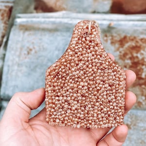 May include: A pink and gold beaded car air freshener shaped like a cow tag.