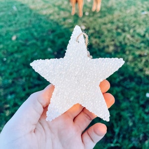 May include: A white star-shaped ornament made of small white beads. The ornament has a string attached to the top for hanging.