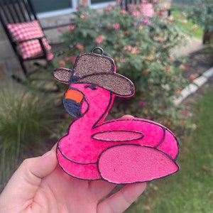 May include: Pink inflatable flamingo pool float with a brown cowboy hat. The flamingo is outlined in black and has a black eye.
