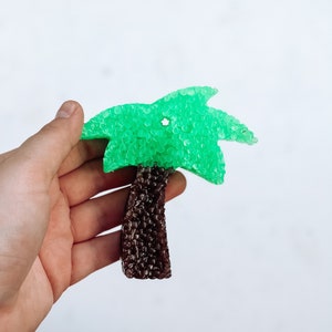 May include: A green palm tree shaped air freshener with a brown trunk. The air freshener is made of small beads.