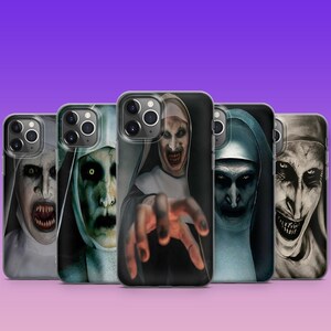 May include: A collection of phone cases featuring a scary nun design. The cases display a variety of images of a demonic nun with a menacing expression, with sharp teeth and reaching hands. The cases are on a gradient purple background.