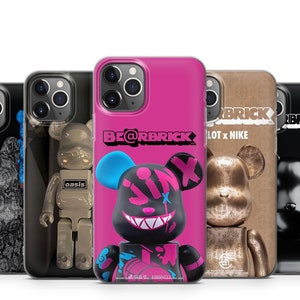 Op de afbeelding: Vier verschillende telefoonhoesjes met het Be@rbrick-logo en verschillende ontwerpen. De hoesjes zijn allemaal zwart en hebben een transparant plastic venster aan de achterkant om de telefoon te laten zien. De ontwerpen omvatten een zwart-witte beer, een gouden beer, een roze beer met een schedelontwerp en een zwarte beer met een schedelontwerp.