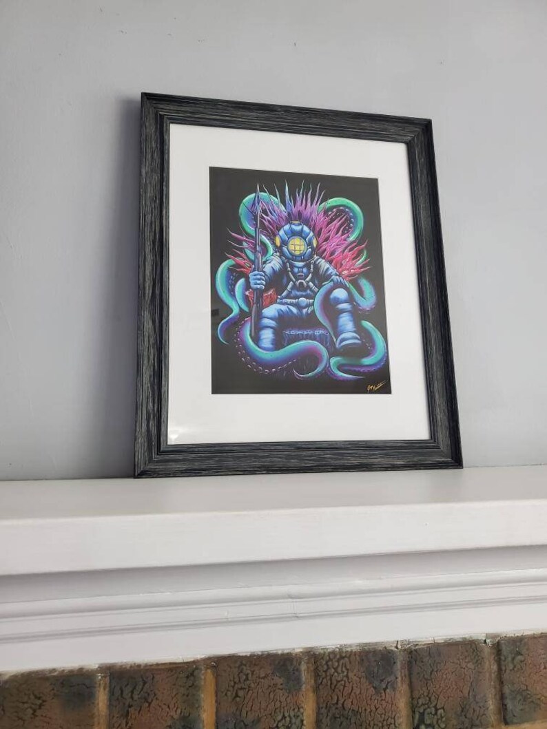May include: Framed art print featuring a diver seated on a throne of tentacles, holding a spear. The diver is in a blue diving suit with a yellow helmet. The artwork has a black background with vibrant teal, purple, and pink accents. The frame is black.