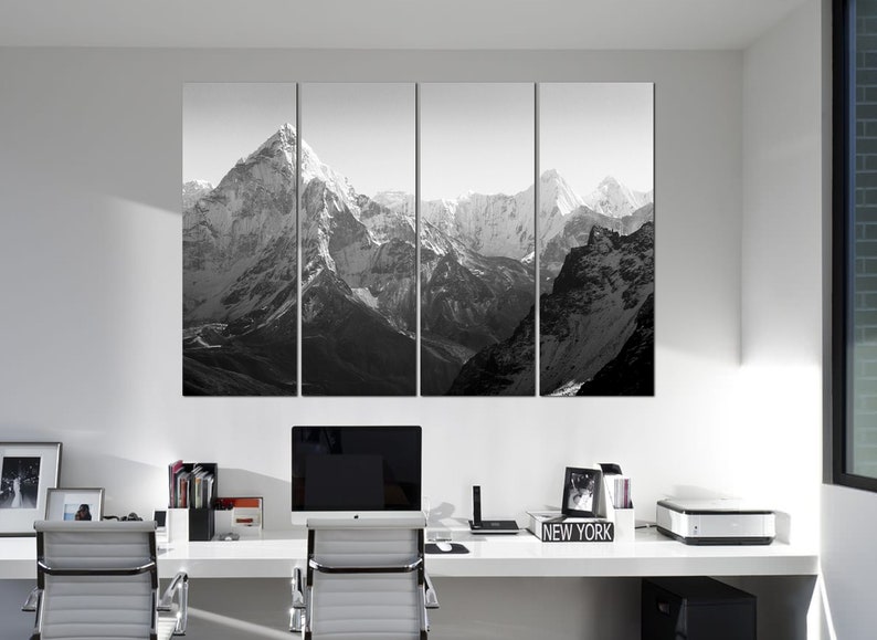 Pu&ograve; includere: Una fotografia in bianco e nero di una catena montuosa con cime innevate. La foto &egrave; divisa in quattro pannelli ed &egrave; esposta su una parete sopra una scrivania con un computer, una stampante e materiale da ufficio.