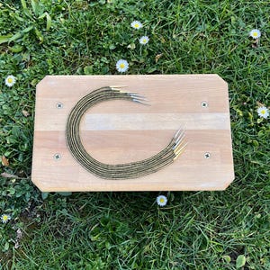 May include: A set of ten black and gold beaded necklaces with gold tips, arranged in a circle on a wooden surface.