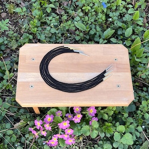 Puede incluir: Un conjunto de siete cordones de cuero negro con puntas plateadas, dispuestos en círculo sobre una superficie de madera.