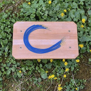 May include: A set of seven blue cords with gold tips, arranged in a circle on a wooden surface.