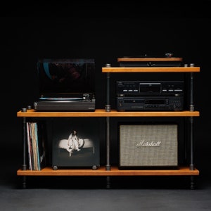 May include: A wooden shelf unit with black metal pipes, holding a turntable, a CD player, a speaker, and vinyl records. The speaker is a Marshall brand and the record is by Billie Eilish.