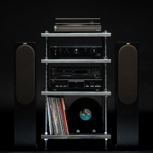 May include: A black audio system featuring a turntable, amplifier, CD player, and vinyl records on a metal shelf unit. Two tall black speakers are positioned on either side. The setup is against a black backdrop.