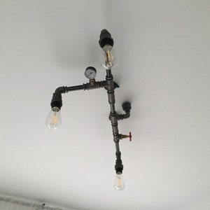 May include: A ceiling light fixture made of black metal pipes with three light bulbs. The fixture has a gauge and a red valve.