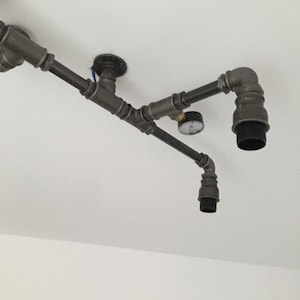 May include: A black industrial style pipe light fixture with two black light sockets and a small gauge attached to the pipe.