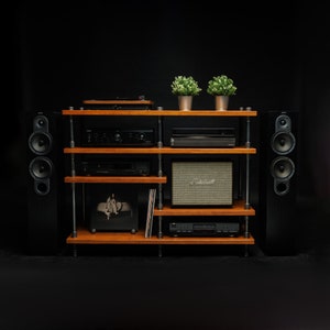 May include: A wooden shelf unit with a black turntable, a black amplifier, a black CD player, a black speaker on each side, and a small black and silver speaker on the middle shelf. The shelf unit has a wooden top and bottom shelf, and metal pipes for the sides and middle shelves.