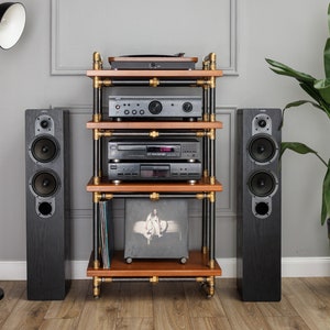 May include: A black wooden stereo shelf unit with four shelves, gold metal pipes, and black wheels. The shelf unit is holding a turntable, amplifier, CD player, and a record. There are two black speakers on either side of the shelf unit. A black floor lamp with a white shade is on the left side of the image. A potted green plant is on the right side of the image.