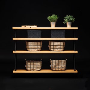 May include: A black metal shelf unit with three wooden shelves. The shelves are filled with black and brown storage baskets. Two potted plants are on the top shelf.