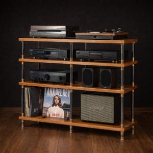 May include: A four-tiered wooden audio rack with black audio equipment, including a turntable, CD players, and an amplifier. Two black speakers and a Marshall speaker are also present. Vinyl records and a record album are visible on the bottom shelf.