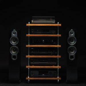 Può includere: Un sistema stereo nero con due grandi altoparlanti su entrambi i lati di un'unità a scaffale in legno. L'unità a scaffale ha cinque ripiani e contiene un giradischi, un lettore CD, un amplificatore e altri componenti audio.