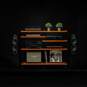 May include: A wooden shelf unit with black speakers on either side. The shelf unit has a record player, a small amplifier, and a record on the top shelf. The shelf unit is against a black background.