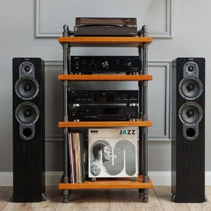 Puede incluir: Un sistema de altavoces estéreo de madera negra con un tocadiscos, un amplificador y un reproductor de CD en un estante de madera con tuberías de metal negro. El estante contiene una pila de discos de vinilo con un disco titulado "JAZZ".