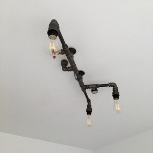 May include: A black metal pipe light fixture with four exposed light bulbs. The fixture is mounted to a white ceiling.