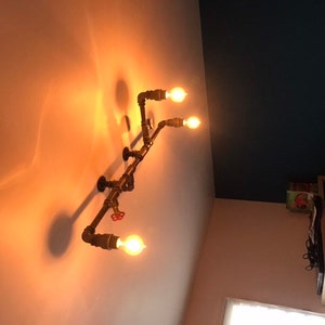 May include: A rustic industrial style light fixture with four exposed light bulbs and a pipe design. The fixture is mounted on a white ceiling.