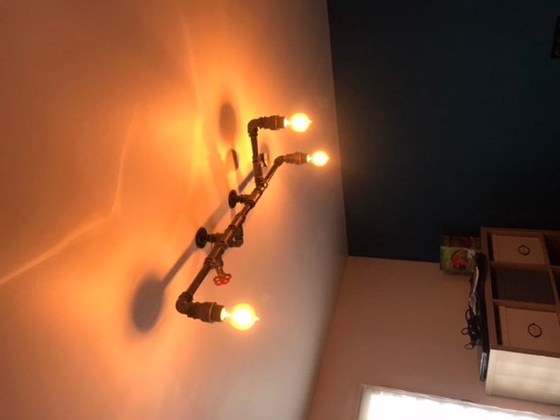 May include: A rustic industrial style light fixture with four exposed light bulbs and a pipe design. The fixture is mounted on a white ceiling.