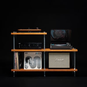 Puede incluir: Una estantería de madera con tres estantes, que presenta un tocadiscos negro, un amplificador negro, un reproductor de discos, un álbum de discos y un altavoz negro y tostado. La estantería está hecha de madera y metal.